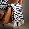 close up image of black and white geometric throw with tassel edges, draped over side of faux brown leather armchair