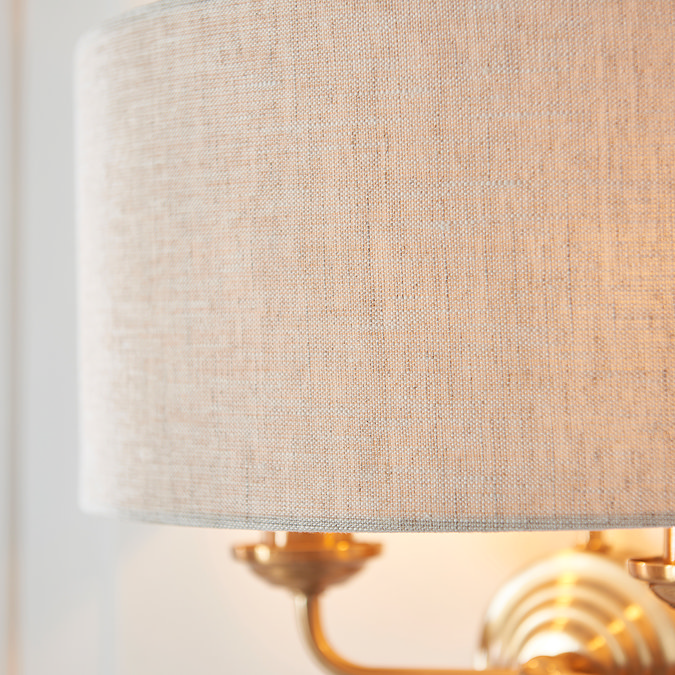 close up on linen shade of vintage brass wall light, emitting a warm glow