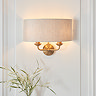 image of vintage brass wall light with linen shade on cream wall with top of potted plant showing underneath