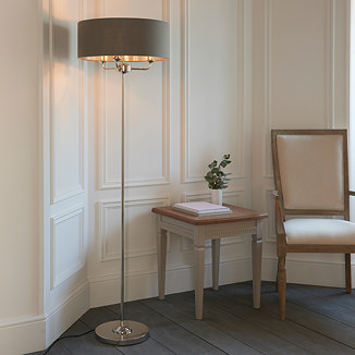 image of tall thin floor lamp with grey shade and nickel body, stood in corner of dining room emitting warm glow