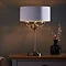 image of antique brass 3 arm table lamp on a bedside table, emitting a warm low against a dark painted wall