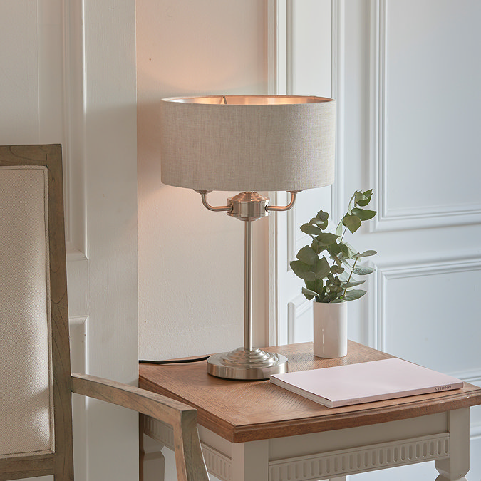 image of table lamp with chrome metalwork body and natural linen shade, on a side table against a cream wall