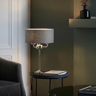 wide shot of nickel and chrome table lamp on a side table with matching ceiling light in a living room with dark green painted walls