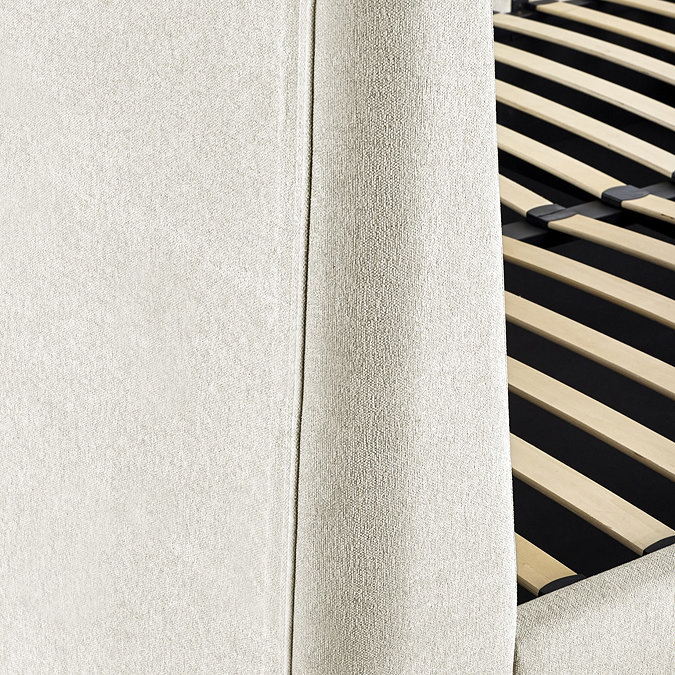 image taken from the back slightly to the side of upholstered beige ottoman bed to show upholstered material and slatted wrack