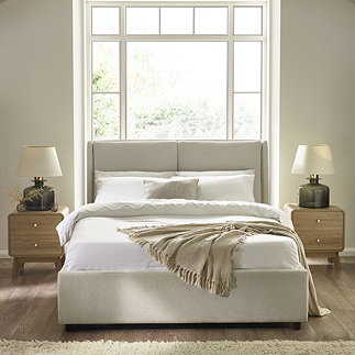 image of beige upholstered double bed with mattress, duvet cover set, and natural throw draped over the end, with light oak bedside tables