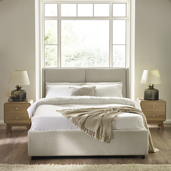 image of beige upholstered double bed with mattress, duvet cover set, and natural throw draped over the end, with light oak bedside tables