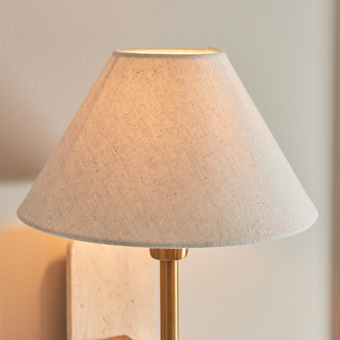 close up image of tapered linen shade of thin brass coloured wall light