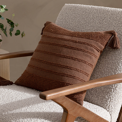 image of brown tasselled square cushion on a boucle armchair