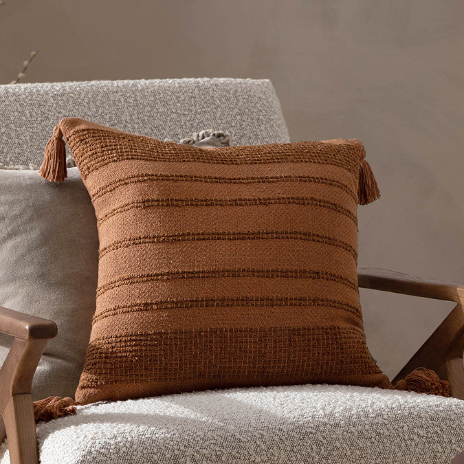 image of square dark orange cushion with tufted stripes across the front and tassels on each corner, on a boucle accent chair
