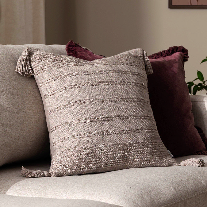 image of stone coloured textured cushion with tasselled corners, on natural sofa in front of burgundy cushion