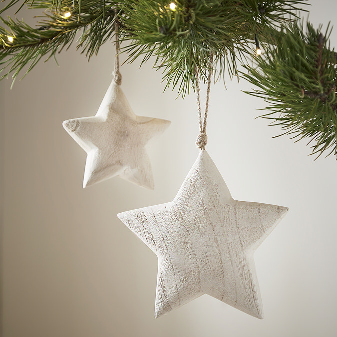 large white wood star hanging from a tree in the foreground, with its smaller counterpart hanging from the tree slightly behind it.