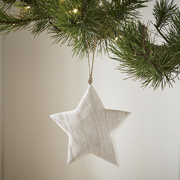 large white wood star hanging from a tree in the foreground, with its smaller counterpart hanging from the tree slightly behind it.