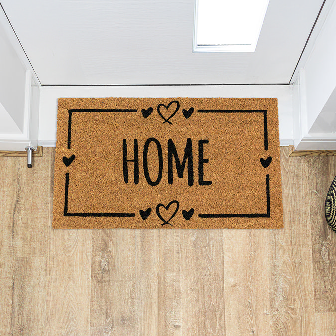 image of rectangular natural doormat with home written in the middle and hearts on the border, on wooden flooring in front of white door