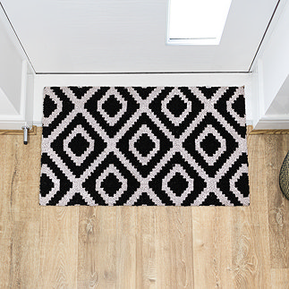 image of rectangular doormat with black and white diamond pattern on wooden flooring in front of white door