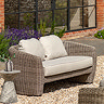 image of rattan two seater sofa with rattan sides and plush cream cushions