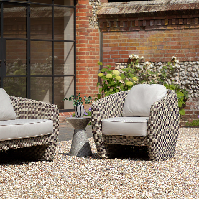 image of single seat rattan garden armchair on gravel back garden, next to small stone side table with matching 2 seat sofa on the other side