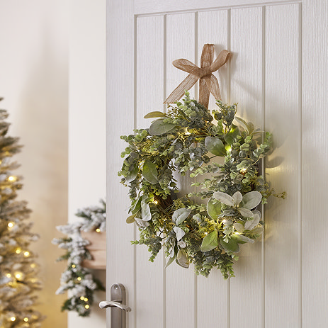 LED eucalyptus and lamb's ear wreath, displayed on the back of a white living room door with a christmas tree blurred in the background to the left