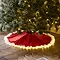 red christmas tree skirt underneath a christmas tree, lit up around its edge by warm white LEDs under its fluffy white trim.