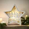 white wooden star with carved intricate scene lit up by LEDs in its middle, placed on a mantlepiece.