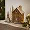 slightly angled photo of wooden house decoration stood on a mantlepiece, next to wooden trees and wooden children figures decorating a snowman