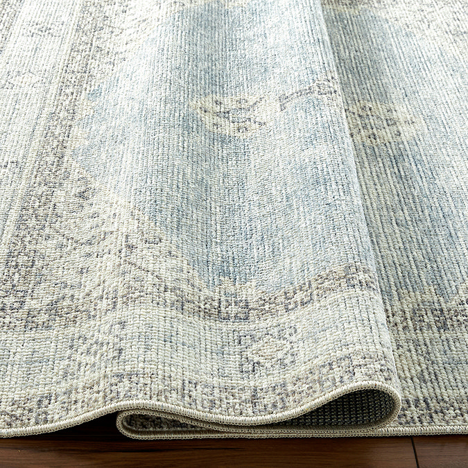 image of vintage patterned blue and white rug ruched up slightly to show its thinness