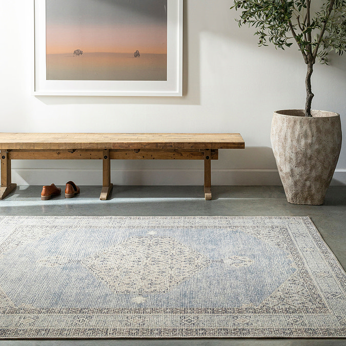 image of blue vintage patterned rug on grey floor in front of oak bench and potted plant