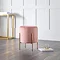 image of pink velvet pouffe with gold accent legs, stood on warm wooden flooring with gold console table in the background