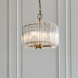 image of glass pendant light in chandelier style with brushed brass support, hanging from ceiling in front of light grey wall