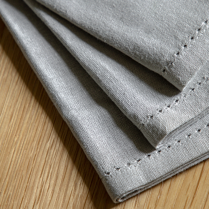 close up image of dotted edged stitching of dove grey linen style napkins on wooden table