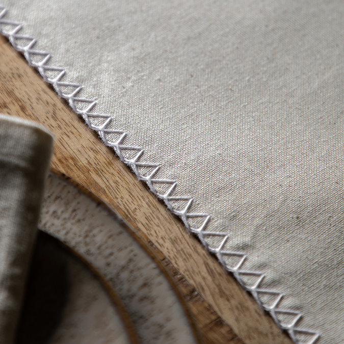 close up image of linen effect table runner with stitched criss-cross edges