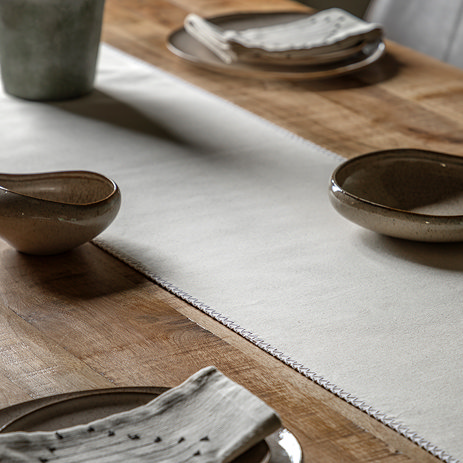 image of cream linen effect table runner across a dark oak dining table, with plates and bowls around it