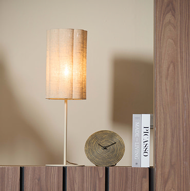 image cut out on white background of linen cylindrical table lamp with bulb emitting a warm glow