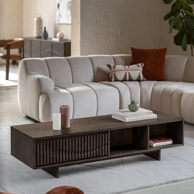 angled image from the side of rectangular walnut coffee table in front of sofa on cream rug, with one drawer and open shelf space