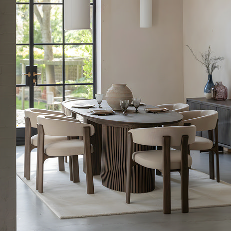 image of large oval walnut coloured dining table with wavy slatted legs and natural chairs tucked in around it