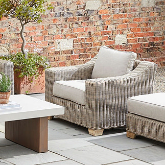 image of rattan outdoor armchair with gentle sloping arms and plush beige cushion, on a patio