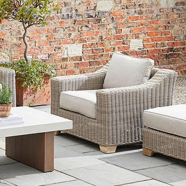 image cut out on white background of beige rattan armchair with plush cushion and light wood feet