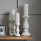 image of three matt white ceramic candle holders in a column-inspired shapes, holding battery-operated candles, on a sideboard