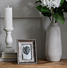 image of small matt white ceramic candle holder in column-inspired design, on top of three books next to a picture frame and stone vase containing a white flower, on top of an oak sideboard