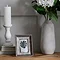 image of small matt white ceramic candle holder in column-inspired design, on top of three books next to a picture frame and stone vase containing a white flower, on top of an oak sideboard