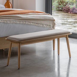 light grey and oak cushioned bench with slim rounded legs at the foot of a bed