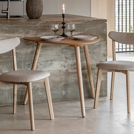 small light oak dining table in curved triangular shape, against a marble side counter with two matching chairs