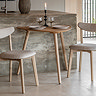 small light oak dining table in curved triangular shape, against a marble side counter with two matching chairs