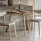 small light oak dining table in curved triangular shape, against a marble side counter with two matching chairs