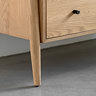 close up on slim foot of 3 drawer chest, made from a light oak coloured material
