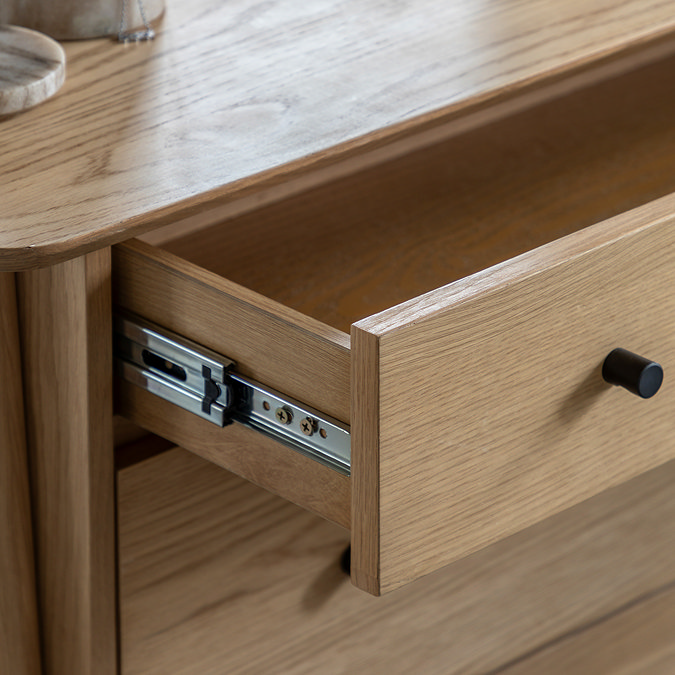 close up on drawer of light oak chest of drawers, pulled out to reveal sliding metal mechanism on side and storage space inside