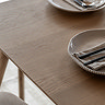 close up image on smooth oak surface of dining table, neutral coloured plates partially in shot
