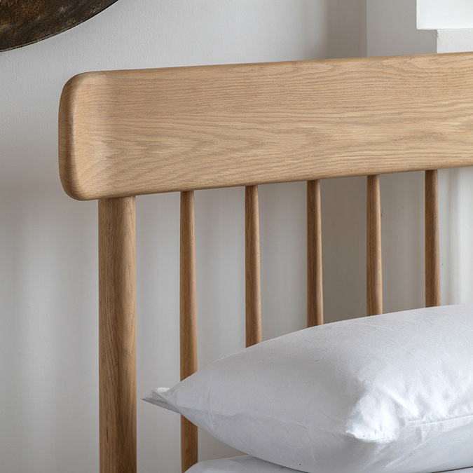 close up on spindled headboard of light oak bed with slightly curved edge