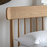 close up on spindled headboard of light oak bed with slightly curved edge