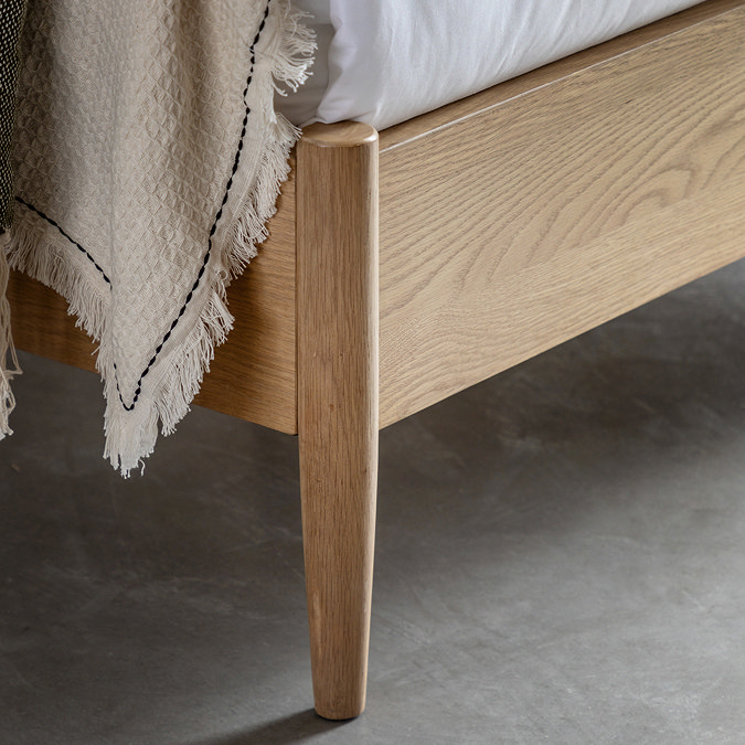 close up on footboard of light oak bed with natural throw thrown slightly over the end and slim feet on grey floor
