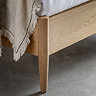 close up on footboard of light oak bed with natural throw thrown slightly over the end and slim feet on grey floor